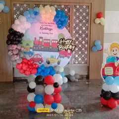 A transportation-themed birthday party for a two-year-old. The round backdrop features a train and cars, surrounded by a colorful balloon arrangement.