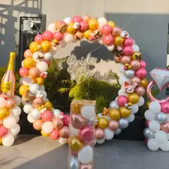 This circular balloon arch was the star of a 'Bride to Be' party. The mix of pink, gold, and white balloons, accented with a neon sign and a champagne bottle balloon, creates a festive and glamorous photo spot.