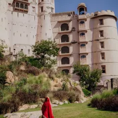 A bride in a traditional red lehenga walks towards the majestic Alila Fort. This single shot tells a story of modern royalty and timeless tradition.