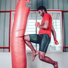 A powerful knee strike is a fundamental weapon in kickboxing and MMA. This photo shows a trainee driving their knee into the heavy bag, a drill that builds core strength and knockout power.