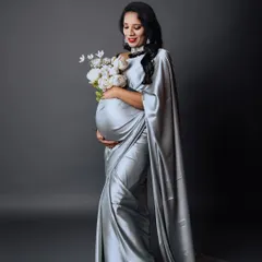 An elegant studio maternity portrait of a mother-to-be in a flowing silver satin saree, holding a bouquet of white flowers. This showcases our ability to create modern, stylish, and sophisticated pregnancy photos.