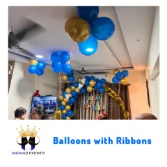 Balloons with ribbons hanging from the ceiling create a fun and celebratory atmosphere. This setup in blue and gold is perfect for a boy's birthday party at home.