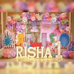 A full and elaborate mermaid-themed stage for a first birthday, featuring a sequin backdrop, light-up letters, and a variety of cute sea animal props like an octopus and crab.