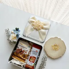 A thoughtful return gift set including a tin of gourmet snacks and a beautiful resin coaster with gold leaf details.