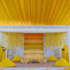 The main stage for the Haldi ceremony, featuring a backdrop of cascading yellow threads in an ombre pattern, flanked by heaps of fresh marigold petals.