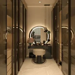 A luxurious walk-in closet with glass doors and integrated lighting. The design includes a central vanity with a backlit mirror, creating a glamorous, boutique-like feel.