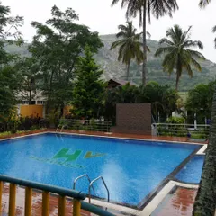 The swimming pool at our Nandi Hills resort, ready for guests to take a dip. The pool area is surrounded by palm trees and offers a view of the hills.