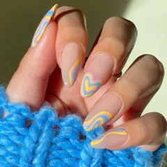 This dreamy, pastel manicure features groovy swirls and a heart-shaped accent nail in shades of yellow, blue, and pink. It's a soft and playful design that's perfect for a whimsical look.