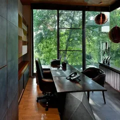 A detail of the cantilevered study, showing the custom-designed desk with its faceted metal base. The minimalist interior ensures that nothing distracts from the primary feature: the floor-to-ceiling view of the lush green canopy outside.