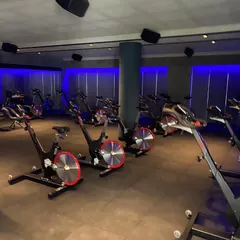 For the Chakra spinning studio, we created a high-energy, immersive environment. The use of dynamic blue ambient lighting against dark walls and industrial-style flooring sets a motivational tone for intense workouts.