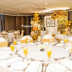 This image shows our birthday backdrop integrated into a full banquet hall setup. We coordinated the elegant gold and white theme of the backdrop with the table settings and chair sashes for a cohesive and upscale event design.