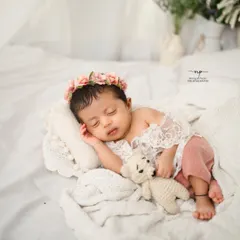 Cuddling a tiny teddy bear, this little one is fast asleep in a sea of soft white blankets. It's a picture of pure innocence.