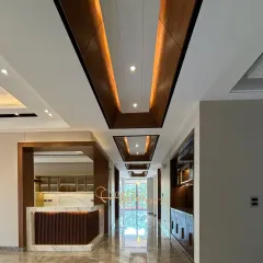 This grand corridor features a striking ceiling design with recessed wood panels and ambient lighting, guiding the eye through the space. The polished marble floor reflects the light, enhancing the sense of luxury.