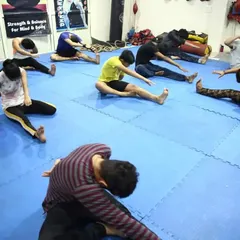 Every session starts with proper conditioning. Here, a group of students performs seated forward bend stretches on the mats to improve flexibility and prevent injuries before their martial arts training begins.