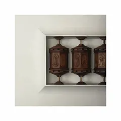 A different perspective of the commissioned prayer wheels. The piece is set within a clean, white niche, allowing the intricate woodwork and craftsmanship of the sculpture to become the sole focus.