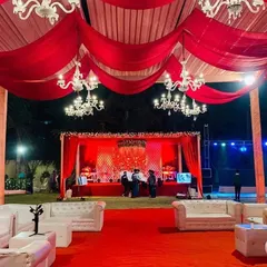 A grand, red-themed reception setup perfect for a sangeet night. The venue is bathed in red light, with large chandeliers, a red carpet, and white lounge sofas creating a luxurious and vibrant party atmosphere.
