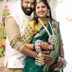 A happy couple at their baby shower. The mom-to-be is adorned in a custom set with purple flowers, featuring a maang tikka, necklace, and matching hand pieces.