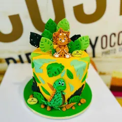 A vibrant 2.5kg dinosaur-themed cake with cute, hand-molded fondant dinosaurs and tropical leaves.