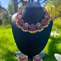 This is a classic Kemp choker with a chandbali design, featuring bright pink stones and green accents. It comes with matching earrings and is perfect for traditional events.