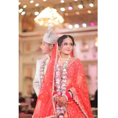 A beautiful portrait of the bride in her red lehenga, with the groom slightly out of focus behind her, creating an artistic shot that highlights her as the star of the moment.