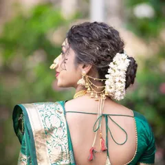 A detailed view of a classic Maharashtrian bridal hairstyle, featuring a curly bun adorned with a gajra and a traditional 'khopa' accessory.