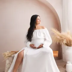 The off-the-shoulder white gown gives this shot a touch of effortless elegance, perfectly complementing the earthy, neutral tones of the studio decor.