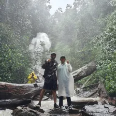 Two trekkers celebrating at the base of Hidlumane Falls, a multi-layered waterfall that is a major highlight of the Kodachadri trek.