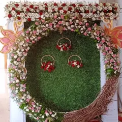 A beautiful floral selfie booth with a green grass backdrop, a large ring of flowers, and smaller hanging floral baskets, designed to be a fun photo spot for guests.