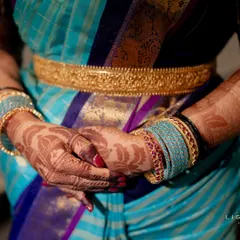 A close-up view of a rich, dark henna stain on the hands. The design features delicate leaf patterns that complement the client's beautiful silk saree and gold vaddanam.