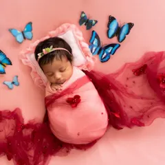 A sweet newborn girl swaddled in pink, surrounded by delicate blue butterflies against a soft pink background. This is a popular fantasy theme for baby girls.