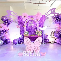 A butterfly theme party featuring a stunning purple sequin wall for a shimmering effect. The setup includes custom butterfly wing cutouts, a themed dessert table, and personalized marquee letters.