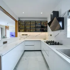 A closer look at the white minimalist kitchen, showcasing the seamless countertops, modern black chimney, and glass-front upper cabinets that add depth and display space.