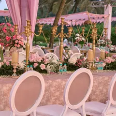 The long dining tables were adorned with golden candelabras and a continuous runner of pink and white flowers. The pink drapes and linens created a soft, romantic atmosphere perfect for a sunset wedding.