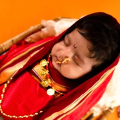 A close-up of a newborn in a traditional Maharashtrian look, dressed in a red nauvari-style wrap with a classic nose ring and bindi.