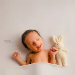 A playful, candid moment with an awake newborn making a funny face next to a small knitted bunny toy. These simple, unposed shots are perfect for capturing your baby's unique quirks.