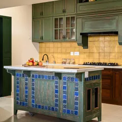 Inspired by the vibrant colors of Goa, this kitchen features a distressed green finish on the cabinetry and a stunning blue tile inlay on the island. The warm yellow handmade tiles on the backsplash add another layer of color and texture. It’s a space that combines the charm of an old-world kitchen with modern functionality.
