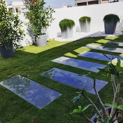 A finished terrace garden project showing a combination of a manicured lawn, modern reflective stepping stones, and carefully chosen potted plants. This design creates a clean, peaceful, and sunny garden space.