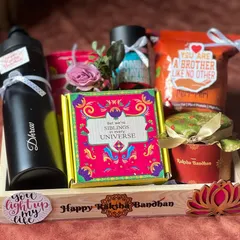 This Rakhi hamper for a brother is curated with a personalized sipper bottle, snacks, and a fun "Siblings in every universe" box, all arranged in a neat wooden tray.