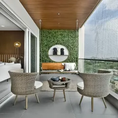 A beautiful and relaxing balcony setup featuring a traditional Indian swing (jhoola) against a green wall. The wicker chairs and safety net make it a perfect family-friendly outdoor space.