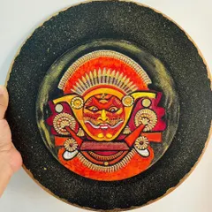 A duplicate image of the Theyyam wall plate, held to show its size and the three-dimensional quality of the painting.