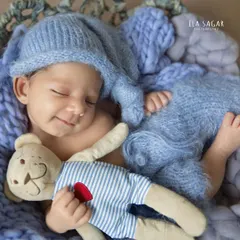 A tiny, sleepy smile from a newborn baby boy. Dressed in soft blue knits and cuddling a teddy bear, this image captures the pure innocence of a new life.