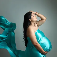 A powerful solo maternity portrait using a vibrant teal fabric wrap. The dramatic lighting and pose create a high-fashion, artistic image that emphasizes the beauty of the female form during pregnancy.