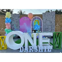 A contemporary outdoor first birthday setup with a large "ONE" table, colorful props, and shimmer wall panels against a stone wall.