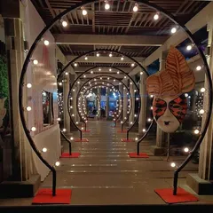 A festive entrance tunnel created for a Christmas event. The series of black arches are lined with lights and decorated with large masks, creating a dramatic and celebratory walkway.