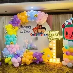 A colorful and fun first birthday party with a Cocomelon theme. The setup features a custom backdrop with characters, a light-up marquee number '1', and a vibrant balloon arch.