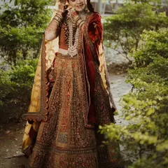 A full-length portrait of a bride in a magnificent red and gold lehenga. The outdoor setting and natural light beautifully complement the richness of her traditional Muslim bridal attire.
