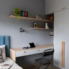 In this kid's bedroom, soothing blues and calming greys create a tranquil color theme. The layout skillfully integrates a bed, a floating study desk, and a full-height wardrobe, making efficient use of space without compromising on style.