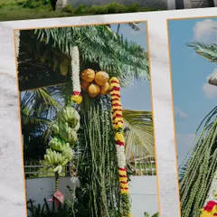 A close-up of a traditional wedding decoration, featuring coconuts and bananas tied to a pillar with vibrant flower garlands, symbolizing prosperity and fertility.
