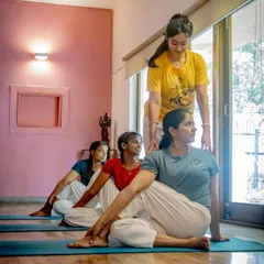 An instructor provides gentle assistance in a seated twist, helping the student find more space and length in her spine while ensuring the posture is performed correctly and safely.