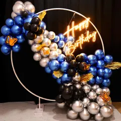 A modern and chic balloon backdrop. This design features a white metal ring frame with a stylish arrangement of blue, black, and silver chrome balloons, accented with gold leaves.